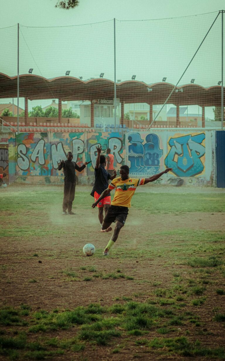 Group of young men playing football on a dusty field with colorful graffiti backdrop.