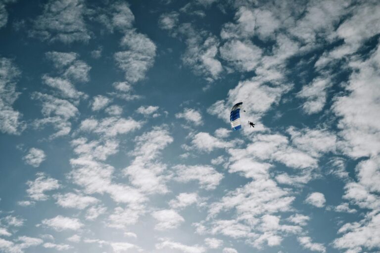 Parachutist gliding through a cloudy blue sky, capturing the thrill of skydiving.