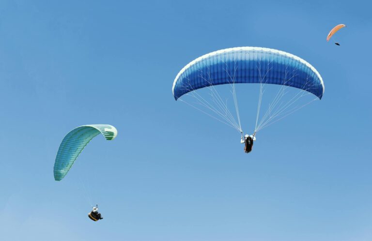 Three paragliders soaring gracefully under a clear blue sky, capturing the essence of adventure.